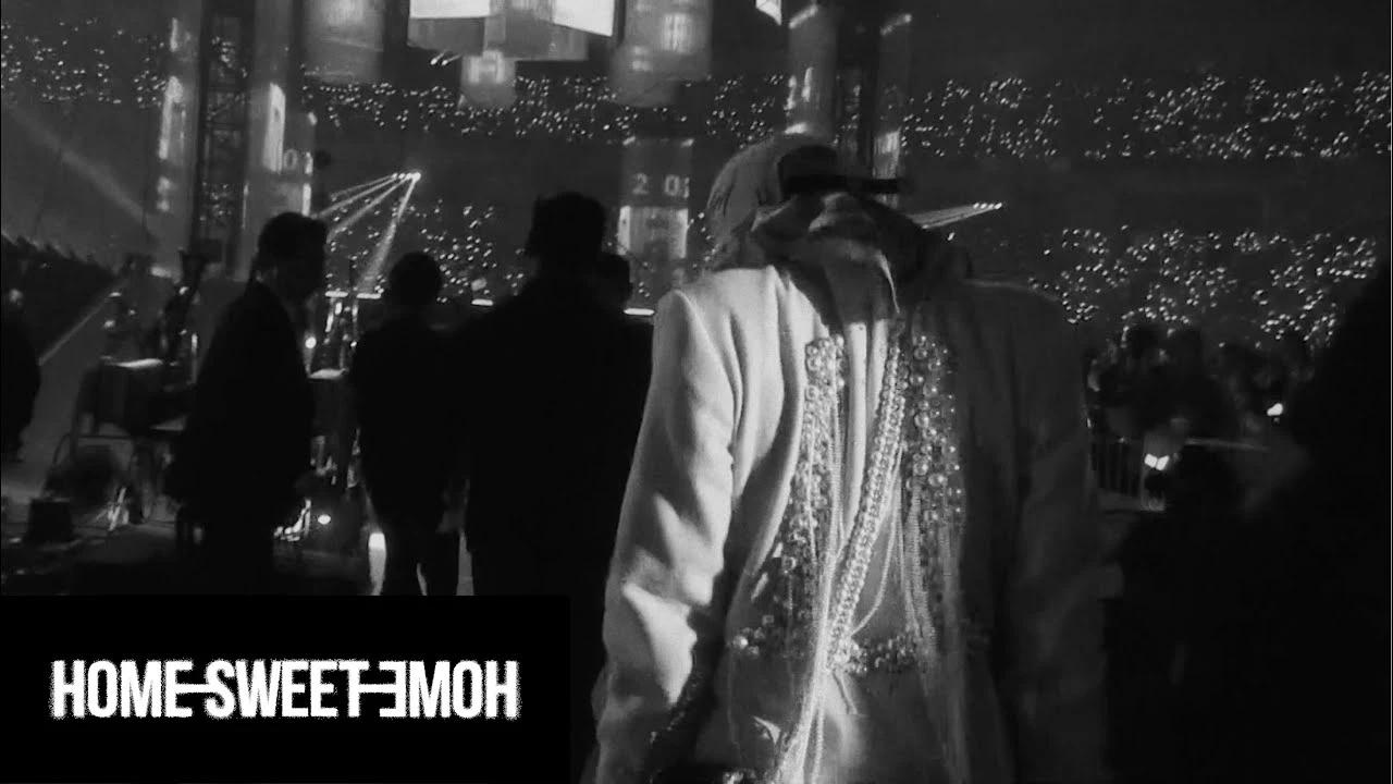 BIGBANG members silhouetted backstage facing a sea of fan lights during their Home Sweet Home era