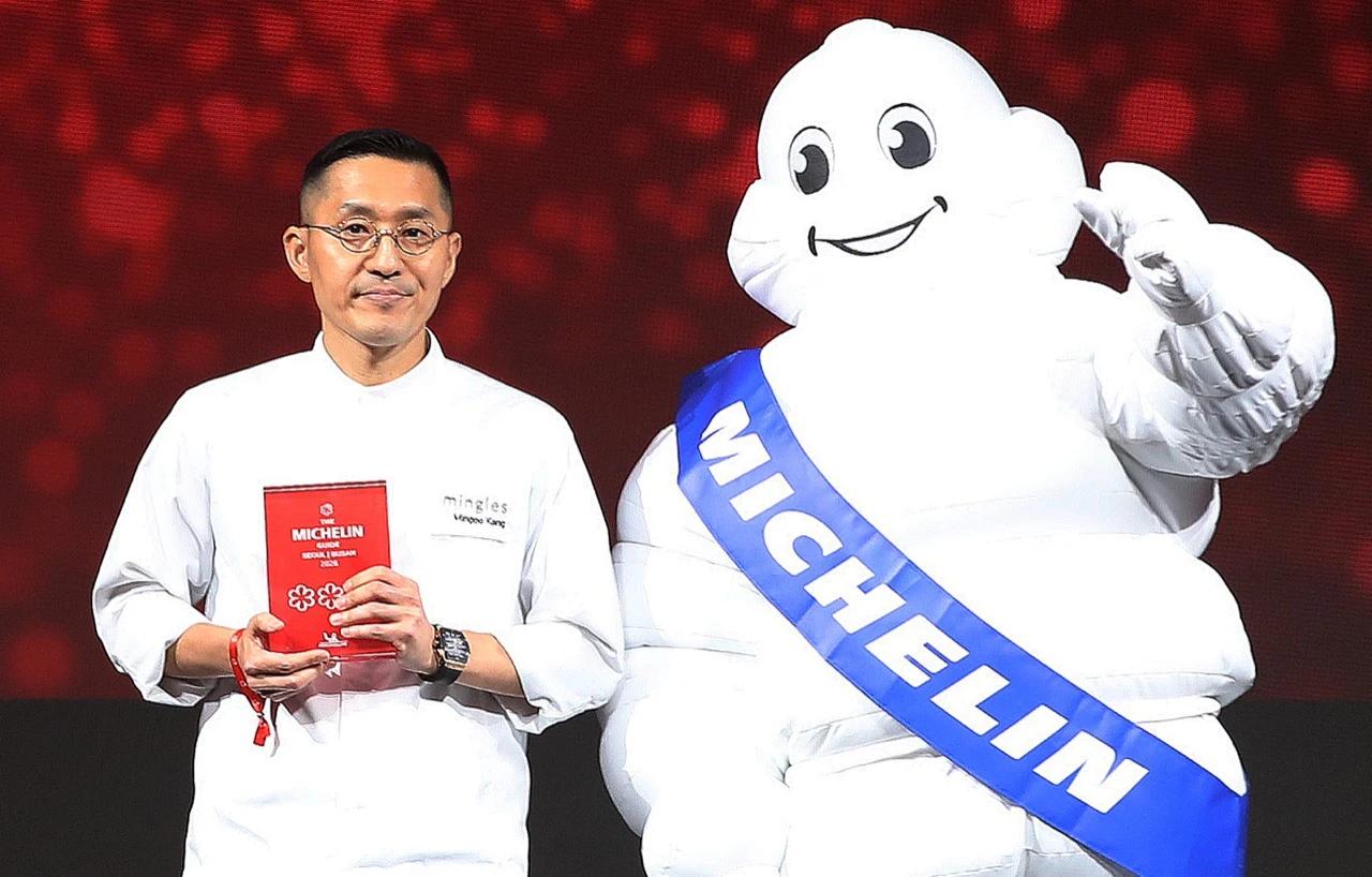 Chef Kang Min-goo of Mingles holding the Michelin Guide Seoul Busan 2026 book at the 10th anniversary ceremony in Busan