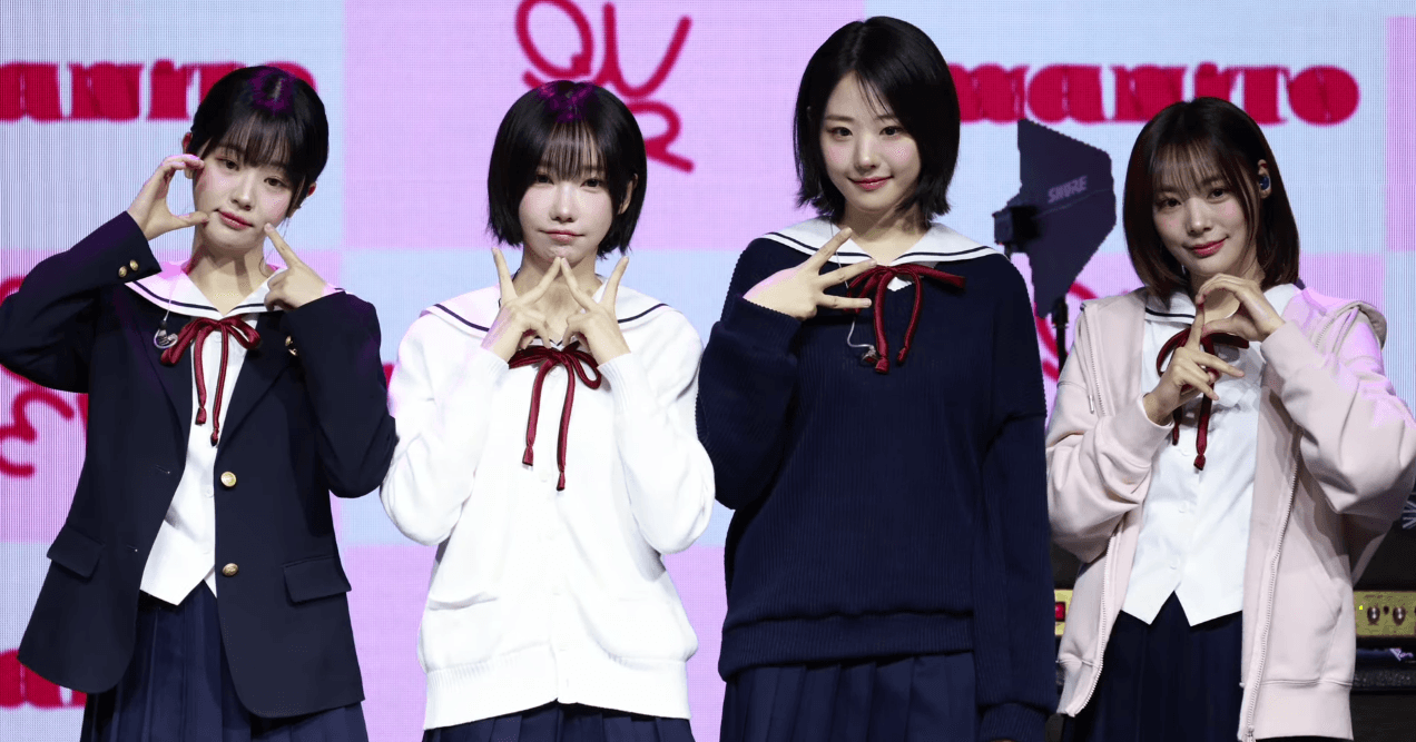 QWER members posing at a showcase with the official QWER logo backdrop