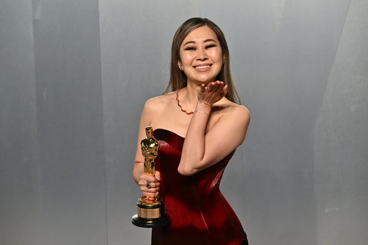 Maggie Kang poses in a red dress while holding an Oscar statuette