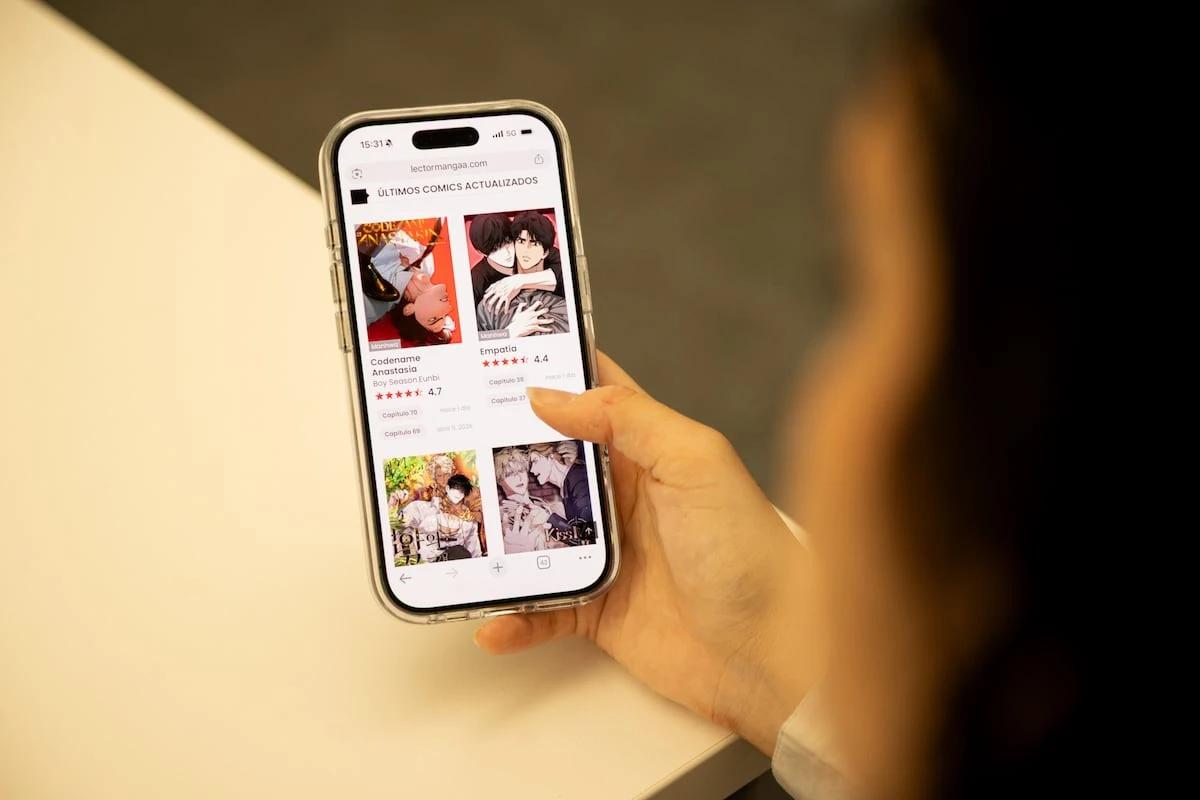 A person holds a smartphone displaying manga and webtoon listings, illustrating the Spanish-language piracy market targeted in the TuMangaOnline crackdown