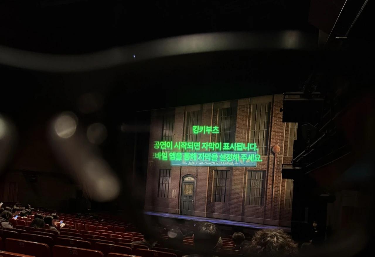 View through AI subtitle glasses inside a theater showing Korean caption overlays above a stage