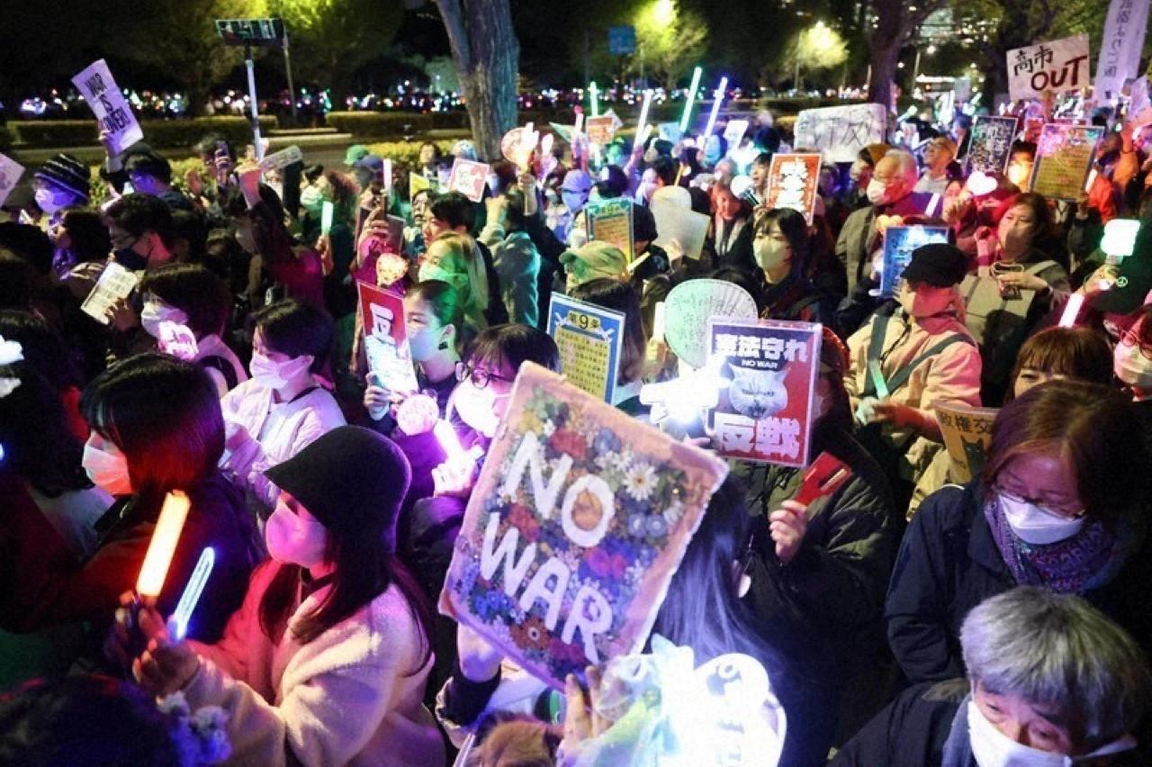 Protesters hold glowing penlights and anti-war signs during a nighttime Tokyo demonstration