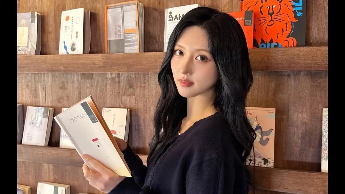 Gaeul stands in front of bookshelves holding an open book in a bookstore-style setting for Reading Korea coverage